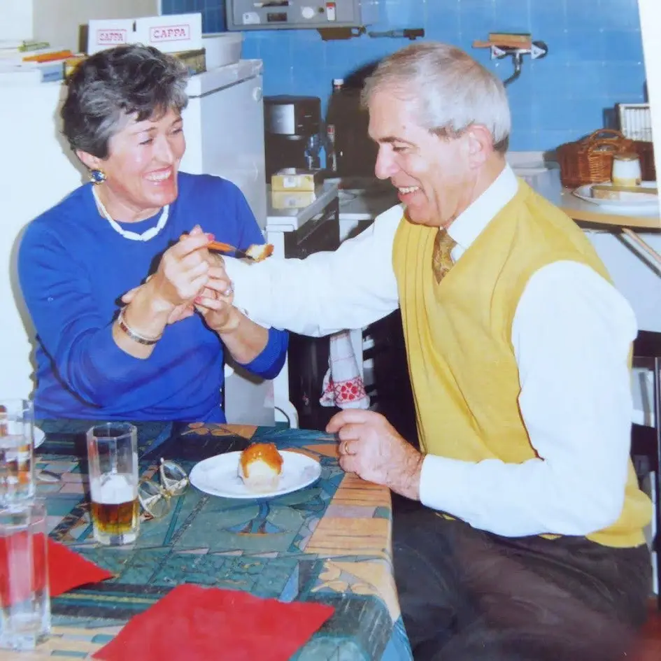 un couple de quinqagénaires souriants se bat pour un baba au rhum dans la cuisine de leur fille