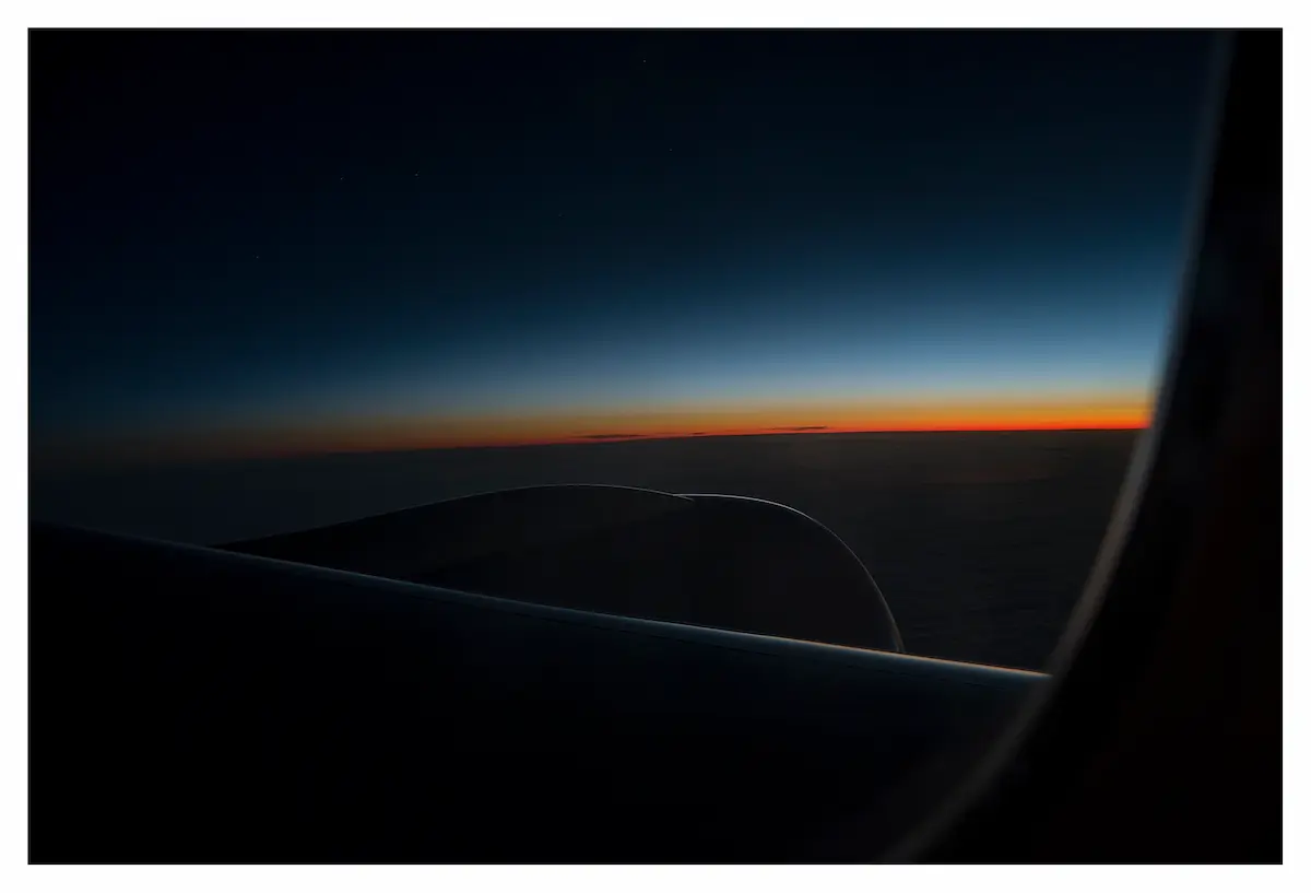 photo poetique prise d'un avion qui capture les couleurs noires bleues jaunes et oranges du lever de soleil dans les airs